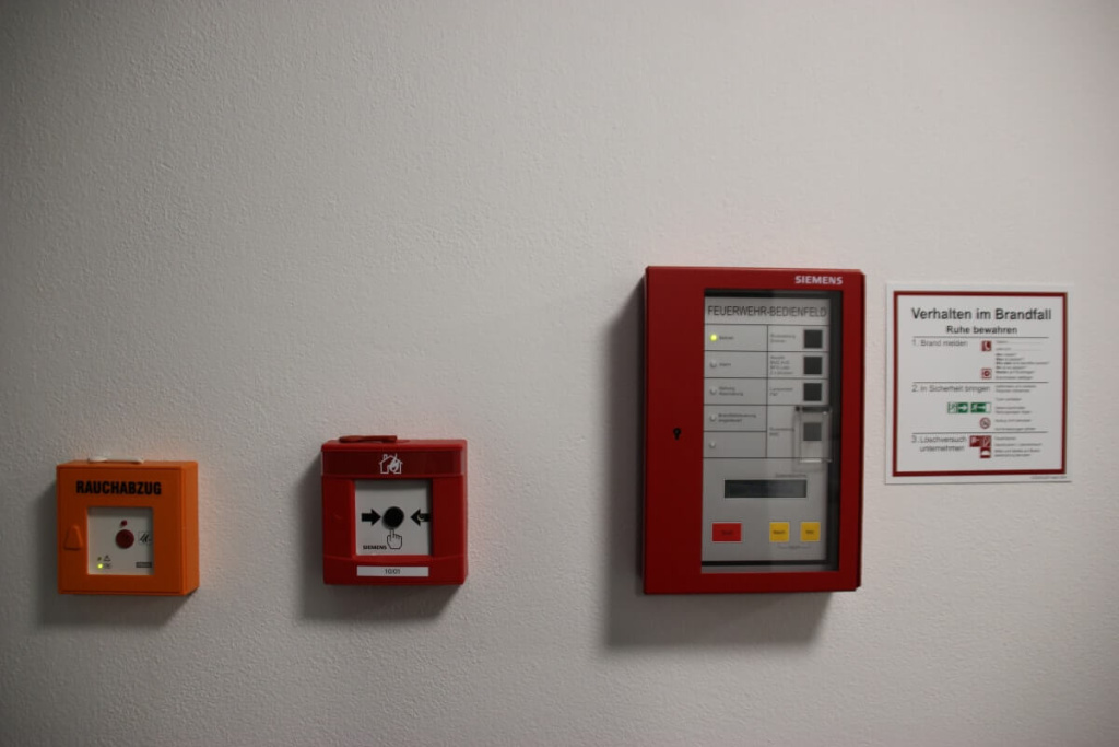 Brandmeldeanlage, Handmelder und Rauchabzug an weißer Wand, Hinweisschild Verhalten im Brandfall