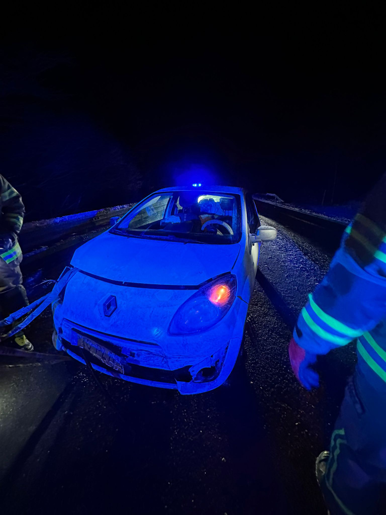 Verkehrsunfall bei Nacht: beschädigter Pkw auf der Straße, Feuerwehrkräfte sichern die Einsatzstelle