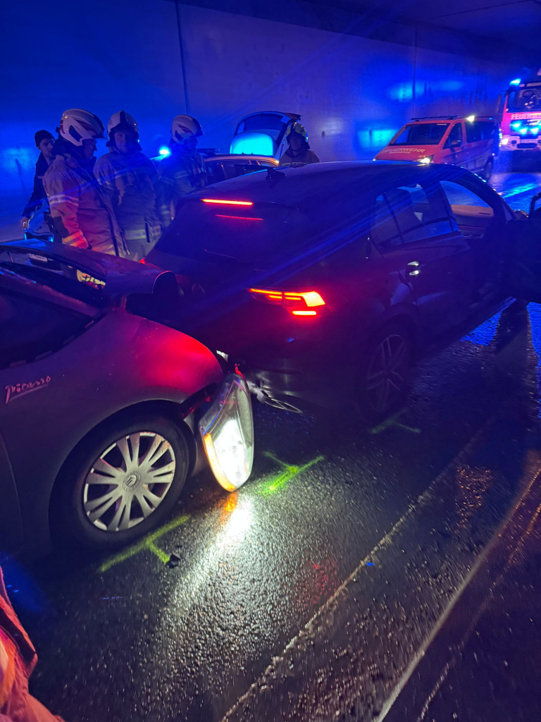 Feuerwehrkräfte sichern einen Verkehrsunfall im Tunnel mit zwei beschädigten Pkw und Blaulicht