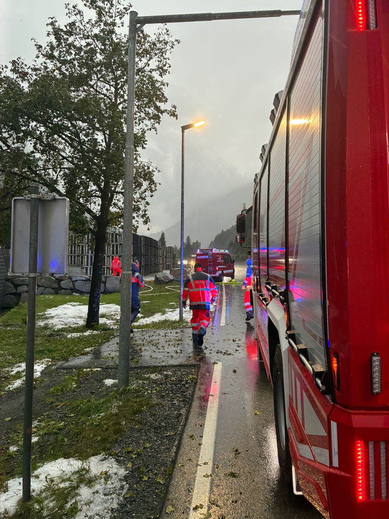 Feuerwehrkräfte bei Starkregen neben Einsatzfahrzeugen auf nasser Straße mit Hagelresten